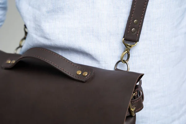 Détails du sac bandoulière en cuir pour homme marron pour un document et un ordinateur portable sur les épaules d'un homme en chemise bleue et un jean avec un fond blanc. Cartable, mallette en cuir pour homme. — Photo
