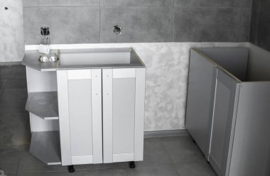 Mobilya cepheli mutfak dolapları döşemesi. Gri modüler mutfak, çeşitli kurulum aşamalarındaki çip malzemelerinden. Bir çerçeve mobilya MDF profilinin önünde.