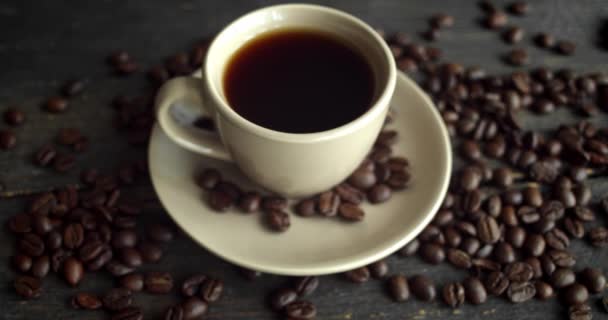 Xícara de café com grãos de café torrados espalhados em uma mesa de madeira. Caneca de café preto fresco. Grãos de café torrados arábica frescos. Grande começo de manhã perfeita. Espresso, americano, doppio. — Vídeo de Stock