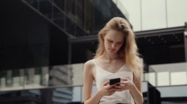 Beyaz tişörtlü genç iş kadını telefon kullanıyor ve iş ortağına ya da iş merkezine ya da alışveriş merkezine sahip arkadaşlarına mesaj yazıyor. Mutlu kız komik bir şey söyler ya da duyar..