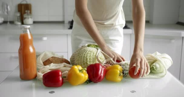 Kadın, alışveriş yaptıktan sonra salatalık ve domatesleri tekrar kullanılabilir market poşetinden alıp evdeki mutfaktaki masada sebzelerle birlikte alıyor. Sıfır atık ve plastiksiz konsept. Pamuk tüccarı. — Stok video