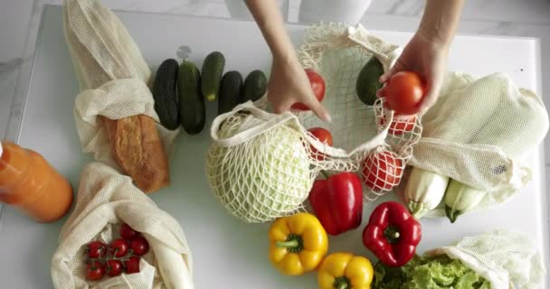 Vrouw haalt tomaten uit herbruikbare boodschappentas met groenten op een tafel in de keuken thuis na boodschappen doen. Geen afval en plastic vrij concept. Mesh katoenshopper. — Stockvideo