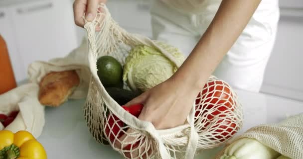 Mujeres con una bolsa de comestibles reutilizable con verduras en una cocina blanca y limpia en casa después de hacer las compras. Cero residuos y concepto libre de plástico. Comprador de algodón de malla con verduras. Ecología. — Vídeos de Stock