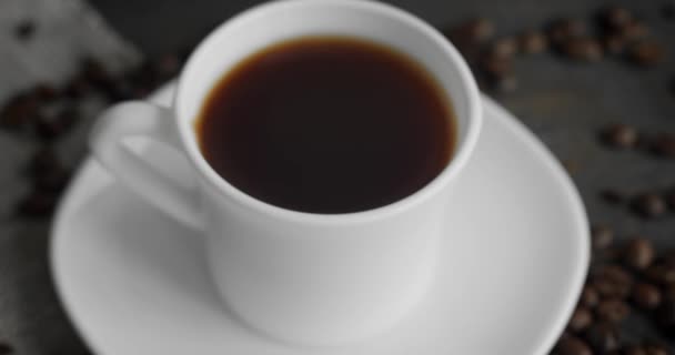 Chávena branca de café com grãos de café torrados espalhados em uma mesa de madeira. Caneca de café preto fresco. Grãos de café torrados arábica frescos. Grande começo de manhã perfeita. Espresso, americano, doppio. — Vídeo de Stock