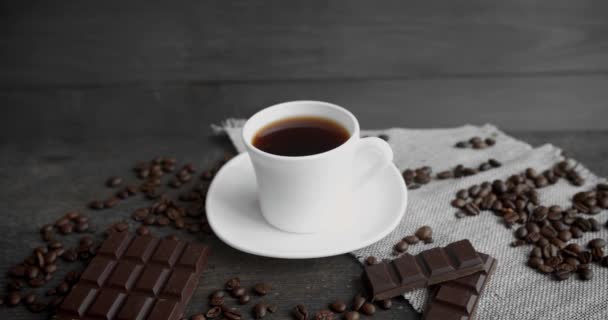 Cup of coffee with chocolate and roasted coffee beans scattered on a wooden table. Black coffee mug. Fresh arabica roasted coffee beans. Great start of morning. Espresso, americano, doppio. — Stock Video