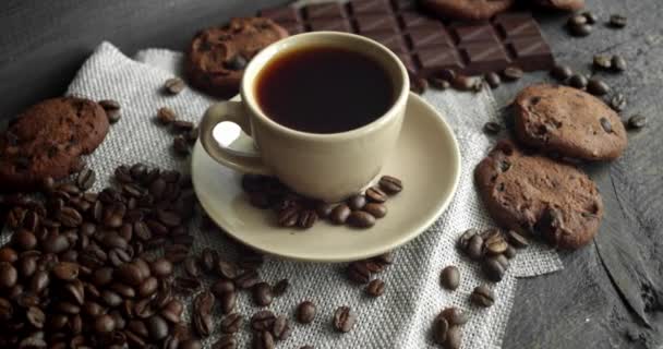 Cup of coffee with cookies, chocolate and roasted coffee beans scattered on a wooden table. Black coffee mug. Fresh arabica roasted coffee beans. Great start of morning. Espresso, americano, doppio. — Stock Video