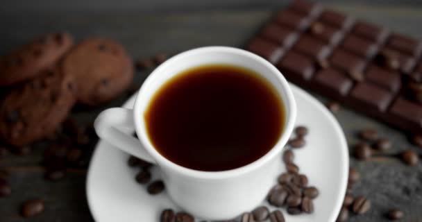 Kopje koffie met koekjes, chocolade en gebrande koffiebonen verspreid over een houten tafel. Zwarte koffiemok. Verse arabica gebrande koffiebonen. Goed begin van de ochtend. Espresso, americano, doppio. — Stockvideo