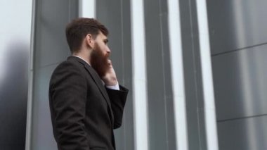 Finans bölgesinde iş adamı telefonda konuşuyor. Ofis binasının üzerinde akıllı telefon kullanan genç bir şehirli adamın portresi. İş adamı dışarıda akıllı telefonuyla konuşuyor. Teknoloji.