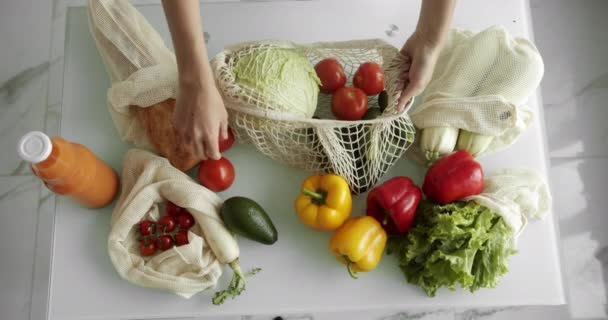 Frau legte ein frisches Gemüse in eine wiederverwendbare Einkaufstasche mit Gemüse auf einen Tisch in der Küche. Null Abfall, plastikfrei, Lebensmitteleinkauf. Mesh-Baumwolleinkäufer. — Stockvideo
