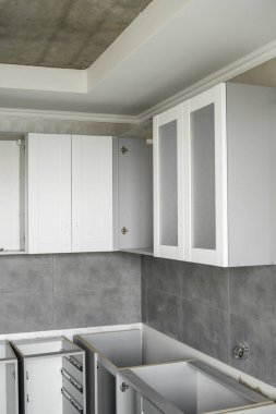 Beyaz mobilya cepheli özel mutfak dolapları kurulumu. Gri modüler mutfak, çeşitli kurulum aşamalarındaki çip malzemelerinden. Bir çerçeve mobilya MDF profilinin önünde.
