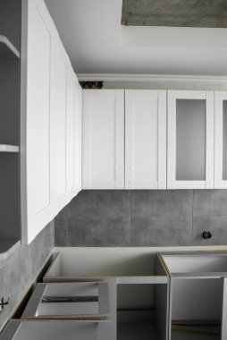 Beyaz mobilya cepheli özel mutfak dolapları kurulumu. Gri modüler mutfak, çeşitli kurulum aşamalarındaki çip malzemelerinden. Bir çerçeve mobilya MDF profilinin önünde.