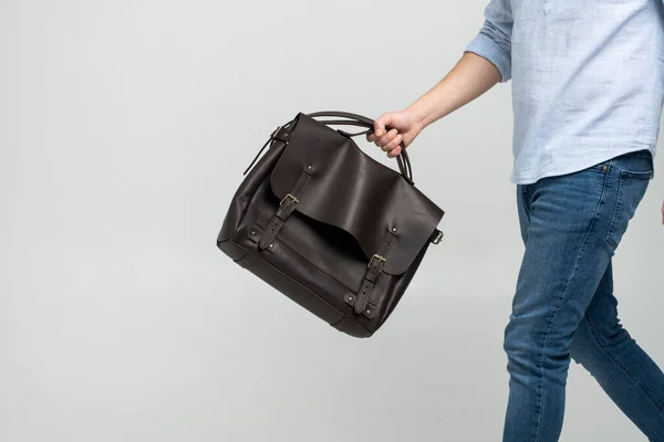 Brązowy męski torba na ramię skórzany dokument i laptop trzymany przez człowieka w niebieskiej koszuli i dżinsy z białym tle. Torebka męska skórzana, ręcznie robiona walizka. — Zdjęcie stockowe