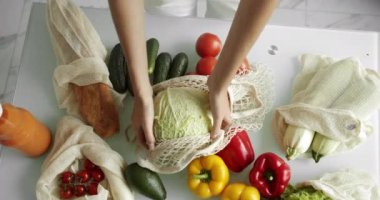 Kadın, sebzeli sebzeli, biberli, domatesli ve salatalıklı lahana paketini mutfaktan çıkartıyor. Sıfır atık, plastiksiz, market alışverişi. Pamuk tüccarı..