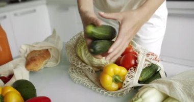 Kadın salatalık ve avokadoyu tekrar kullanılabilir market çantasına koydu. Sebzeli ve biberli masaya, domatesli mutfağa. Sıfır atık, plastiksiz, market alışverişi. Pamuk tüccarı..