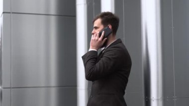 Finans bölgesinde iş adamı telefonda konuşuyor. Ofis binasının üzerinde akıllı telefon kullanan genç bir şehirli adamın portresi. İş adamı dışarıda akıllı telefonuyla konuşuyor. Teknoloji.