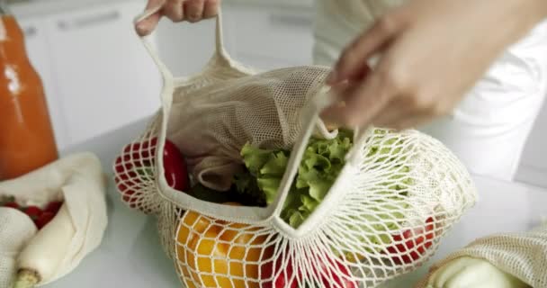 Vrouwen met een herbruikbare boodschappentas met groenten op een witte schone keuken thuis na het boodschappen doen. Geen afval en plastic vrij concept. Mesh katoenen shopper met groenten. Ecologie. — Stockvideo