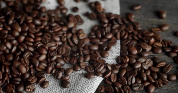 Grãos de café espalhados de uma bolsa de linho em uma mesa de madeira. Grãos de café arábica torrados frescos. Espresso, americano, doppio, cappuccino, latte. Robusta. Foco seletivo. — Vídeo de Stock