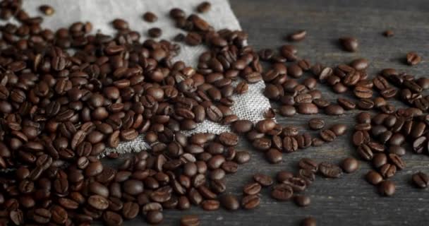 Kávová zrna roztroušená z plátěného pytle na dřevěném stole. Čerstvé pražené arabské kávové zrno. Espresso, americano, doppio, cappuccino, latte. Robusto. Selektivní zaměření. — Stock video