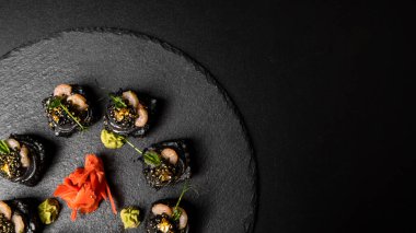 Suşi, siyah pirinç, yengeç eti, salatalık, avokado, tütsülenmiş somon balığı, kürek havyarı, masago, karides kokteyli ve kırmızı zencefil ve wasabi soslu yenilebilir altın yaprak..