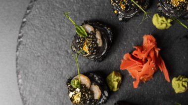 Suşi, siyah pirinç, yengeç eti, salatalık, avokado, tütsülenmiş somon balığı, kürek havyarı, masago, karides kokteyli ve kırmızı zencefil ve wasabi soslu yenilebilir altın yaprak..