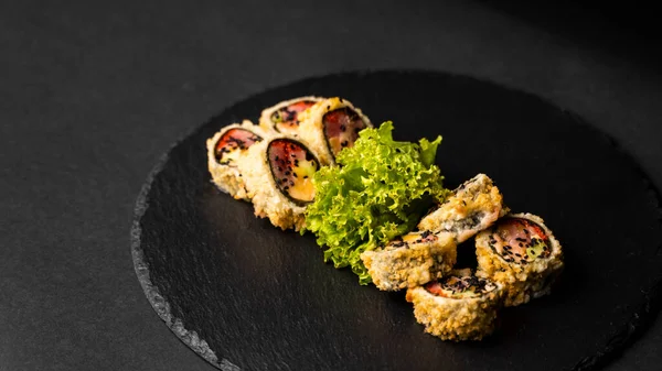 Custom sushi roll w tempura z nori, świeżego łososia, tuńczyka, awokado, kawior masago, skropione sosem ananasowym z sałatką wylewania jako dekoracji na czarnej płycie na czarnym stole i tle. — Zdjęcie stockowe