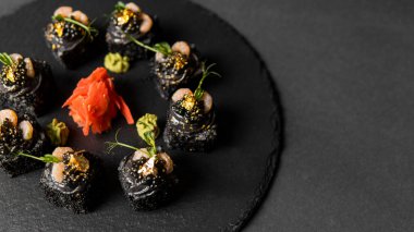Suşi, siyah pirinç, yengeç eti, salatalık, avokado, tütsülenmiş somon balığı, kürek havyarı, masago, karides kokteyli ve kırmızı zencefil ve wasabi soslu yenilebilir altın yaprak..