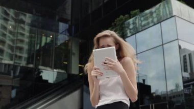 Beyaz tişörtlü bir iş kadını portresi gülüyor ve arkasında iş merkezi olan bir tablet bilgisayar tutuyor. Toplantı ve iş ortağı bekleyen mutlu genç bir kadın..