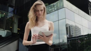 Beyaz tişörtlü bir iş kadını portresi arkasında iş merkezi olan bir tablet bilgisayar kullanıyor. İş kadını iş ortağıyla buluşuyor, iş ortağı bekliyor ve elinde bir tablet tutuyor..