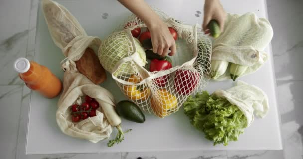 La mujer saca los pepinos de la bolsa de la compra reutilizable con hortalizas en la mesa en la cocina en casa después de la compra. Cero residuos y concepto libre de plástico. Comprador de algodón de malla. — Vídeos de Stock