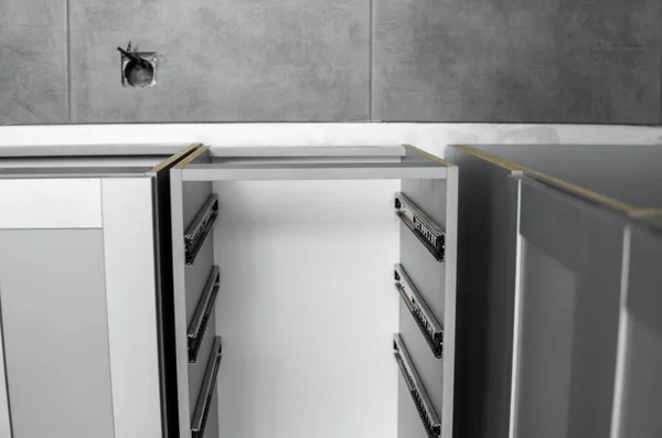 Ausziehbare Schubladenführungen aus rostfreiem Bajonett, montiert auf einem Küchenschrank aus grauer Spanplatte. Zubehör für Tischlerarbeiten, die im Möbelbau verwendet werden. Maßgeschneiderte Küche. — Stockfoto