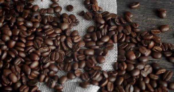 Grãos de café espalhados de uma bolsa de linho em uma mesa de madeira. Grãos de café arábica torrados frescos. Espresso, americano, doppio, cappuccino, latte. Robusta. Foco seletivo. — Vídeo de Stock