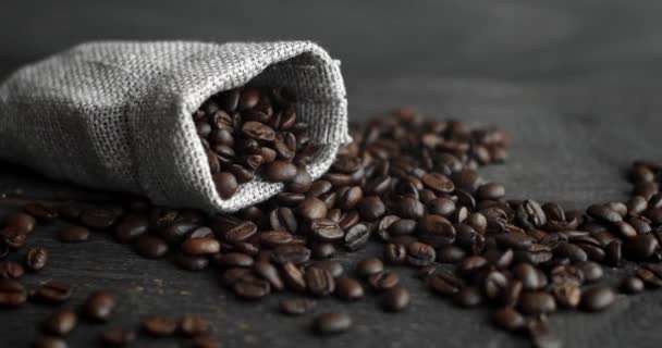 Granos de café esparcidos de una bolsa de lino en una mesa de madera. Granos de café arábica recién asados. Espresso, americano, doppio, capuchino, latte. Robusta. Enfoque selectivo. — Vídeo de stock