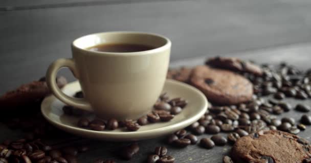 Kopp kaffe med kakor och rostade kaffebönor utspridda på ett träbord. Svart kaffemugg. Färska arabica rostade kaffebönor. Bra början på morgonen. Espresso, americano, doppio. — Stockvideo