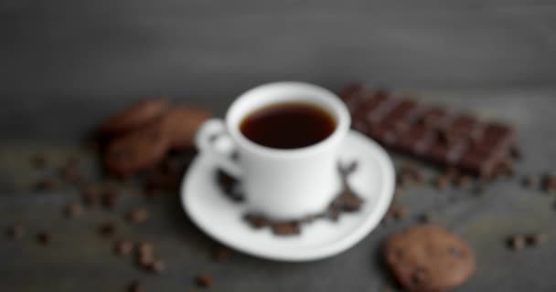 Xícara de café com biscoitos, chocolate e grãos de café torrados espalhados em uma mesa de madeira. Caneca de café preta. Grãos de café torrados arábica frescos. Bom começo de manhã. Espresso, americano, doppio. — Vídeo de Stock