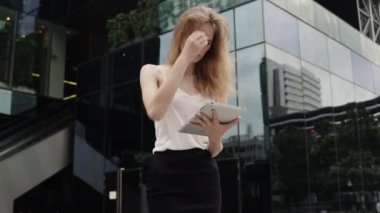 Beyaz tişörtlü bir iş kadını portresi arkasında iş merkezi olan bir tablet bilgisayar kullanıyor. İş kadını iş ortağıyla buluşuyor, iş ortağı bekliyor ve elinde bir tablet tutuyor..