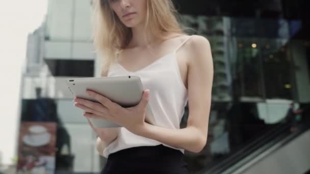 Πορτρέτο της επιχειρηματία σε ένα λευκό t-shirt χρησιμοποιεί έναν υπολογιστή tablet με ένα επιχειρηματικό κέντρο πίσω, εξωτερική. Επιχειρηματίας σε μια συνάντηση και περιμένει επιχειρηματικό εταίρο και κρατώντας ένα δισκίο στα χέρια. — Αρχείο Βίντεο