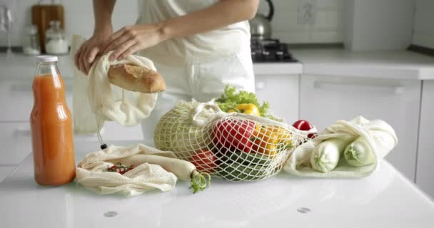 Vrouwen met een herbruikbare boodschappentas met groenten op een witte schone keuken thuis na het boodschappen doen. Geen afval en plastic vrij concept. Mesh katoenen shopper met groenten. Ecologie. — Stockvideo