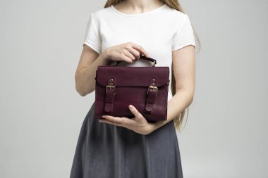 Beyaz arka planda bir kadının elinde küçük kırmızı deri bir çanta. Omuz çantası. Beyaz gömlekli, gri etekli ve kırmızı çantalı bir kadın. Tarz, retro, moda, klasik ve zarafet.