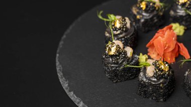 Suşi, siyah pirinç, yengeç eti, salatalık, avokado, tütsülenmiş somon balığı, kürek havyarı, masago, karides kokteyli ve kırmızı zencefil ve wasabi soslu yenilebilir altın yaprak..