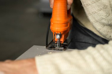 Özel mutfak dolabının arkasındaki fiberboard 'u kesmek için elektrikli yapboz kullanan bir adam eli. Mutfak kurulumu. Profesyonel el testereli bir marangoz..