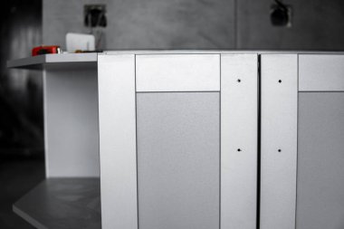 Mobilya cepheli mutfak dolapları döşemesi. Gri modüler mutfak, çeşitli kurulum aşamalarındaki çip malzemelerinden. Bir çerçeve mobilya MDF profilinin önünde.