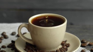 Bir damla kahve bej bir fincan espresso düşürür kahve çekirdekleri masaya saçılmış ve ahşap bir masanın üzerine keten bir bez parçası. Taze lezzetli kahve içilmeye hazır..