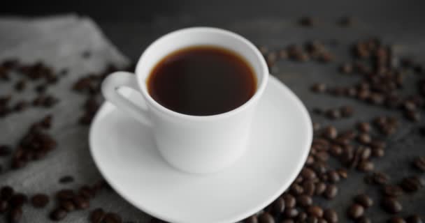 White cup of coffee with roasted coffee beans scattered on a wooden table. Mug of fresh black coffee. Fresh arabica roasted coffee beans. Great start of perfect morning. Espresso, americano, doppio. — Stock Video