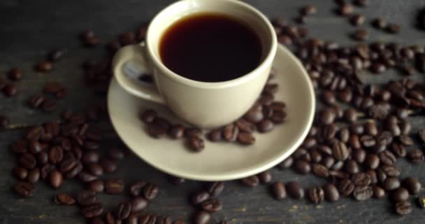 Cup of coffee with roasted coffee beans scattered on a wooden table. Mug of fresh black coffee. Fresh arabica roasted coffee beans. Great start of perfect morning. Espresso, americano, doppio. — Stock Video