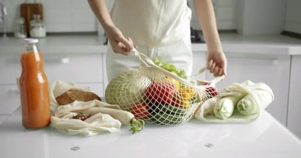 Mujeres con una bolsa de comestibles reutilizable con verduras en una cocina blanca y limpia en casa después de hacer las compras. Cero residuos y concepto libre de plástico. Comprador de algodón de malla con verduras. Ecología. — Vídeos de Stock