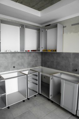 Mobilya cepheleri olmadan özel mutfak dolapları kurulumu. Mutfakta, zemin ve duvarlarda gri fayanslar bulunan çeşitli kurulum aşamalarındaki yonga malzemelerinden gri modüler mutfak..