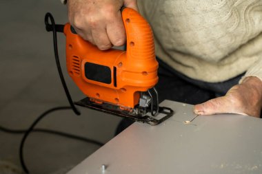 Özel mutfak dolabının arkasındaki fiberboard 'u kesmek için elektrikli yapboz kullanan bir adam eli. Mutfak kurulumu. Profesyonel el testereli bir marangoz..