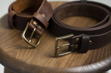 Tahta koltukta bronz tokalı iki kahverengi deri erkek kemeri ve beyaz bir arka plan. El yapımı deri kemer..