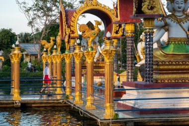 KOH SAMUI, THAILAND - 10 Ocak 2020: Koh Samui thailand 'daki Wat plai laem tapınağındaki dev renkli Buda heykelinin köprüsünde duran kırmızı elbiseli kadın.