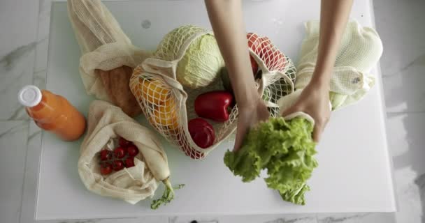 女人把新鲜的沙拉放在一个可重复使用的购物袋里，在厨房的桌上放上新鲜蔬菜。零浪费，无塑料概念，杂货店购物。网状棉织物购物者. — 图库视频影像